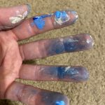 The artists hands showing the fingers covered in many shades of blue paint going down to the second knuckle